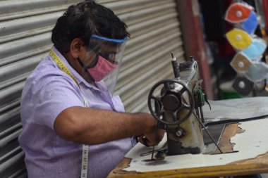 Hyderabad, Telangana, Hindistan. Temmuz-19-2020: terzi koruyucu yüz maskesi takarken giysileri tamir etmek, dikmek ve ayarlamak içindir. Yüzünde güvenlik maskesi olan bir adam, salgın konsepti.
