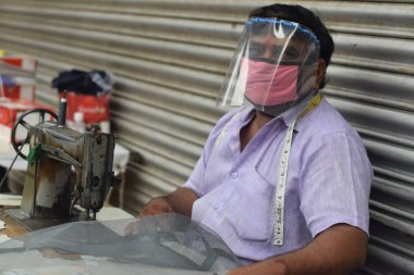Hyderabad, Telangana, Hindistan. Temmuz-19-2020: terzi koruyucu yüz maskesi takarken giysileri tamir etmek, dikmek ve ayarlamak içindir. Yüzünde güvenlik maskesi olan bir adam, salgın konsepti.