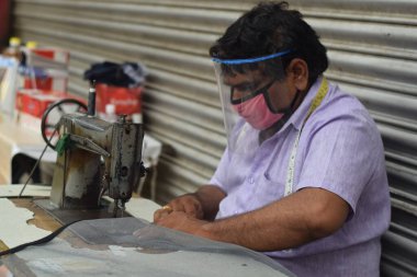 Hyderabad, Telangana, Hindistan. Temmuz-19-2020: terzi koruyucu yüz maskesi takarken giysileri tamir etmek, dikmek ve ayarlamak içindir. Yüzünde güvenlik maskesi olan bir adam, salgın konsepti.