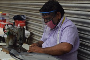 Hyderabad, Telangana, Hindistan. Temmuz-19-2020: terzi koruyucu yüz maskesi takarken giysileri tamir etmek, dikmek ve ayarlamak içindir. Yüzünde güvenlik maskesi olan bir adam, salgın konsepti.