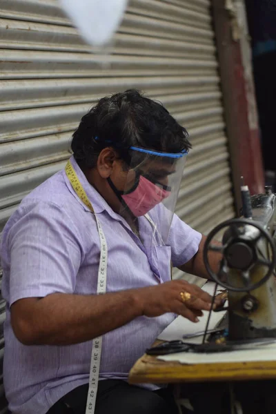 Hyderabad, Telangana, Hindistan. Temmuz-19-2020: terzi koruyucu yüz maskesi takarken giysileri tamir etmek, dikmek ve ayarlamak içindir. Yüzünde güvenlik maskesi olan bir adam, salgın konsepti.