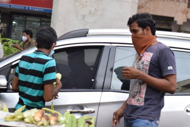 Hyderabad, Telangana, Hindistan. Temmuz-20-2020: Kızarmış mısır, insanlar yüz maskesi takarak işlerini yapıyorlar, arabaya binen kişi bir maske satın alıyor