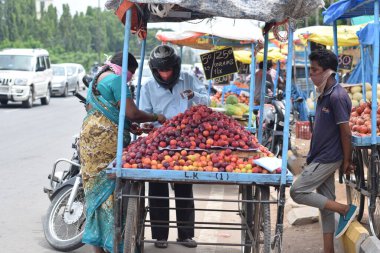 Hyderabad, Telangana, Hindistan. Temmuz-22-2020: Meyveler yol kenarında, meyve tüccarı yol kenarında meyve satarken koronavirüsten korunmak için maske takıyor, korona salgını zamanı, insanlar meyve alırken koruyucu maskeler takıyor
