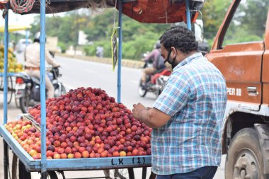Hyderabad, Telangana, Hindistan. Temmuz-22-2020: Meyveler yol kenarında, meyve tüccarı yol kenarında meyve satarken koronavirüsten korunmak için maske takıyor, korona salgını zamanı, insanlar meyve alırken koruyucu maskeler takıyor