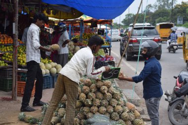 Hyderabad, Telangana, Hindistan. Temmuz-22-2020: Meyveler yol kenarında, meyve tüccarı yol kenarında meyve satarken koronavirüsten korunmak için maske takıyor, korona salgını zamanı, insanlar meyve alırken koruyucu maskeler takıyor