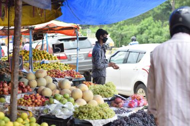 Hyderabad, Telangana, Hindistan. Temmuz-22-2020: Meyveler yol kenarında, meyve tüccarı yol kenarında meyve satarken koronavirüsten korunmak için maske takıyor, korona salgını zamanı, insanlar meyve alırken koruyucu maskeler takıyor