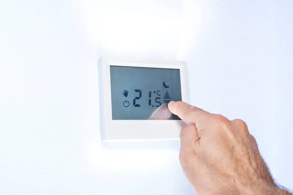 Hand press indoor room thermostat to lower the temp, Stock image