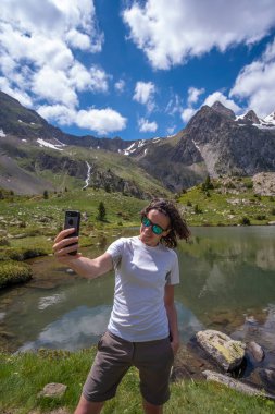 Buzul gölü üzerinde akıllı telefonuyla selfie çeken bir kadın.