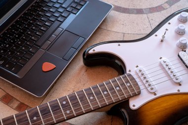 Elektro gitar, internetten gitar dersi alan bir dizüstü bilgisayarın yanında.
