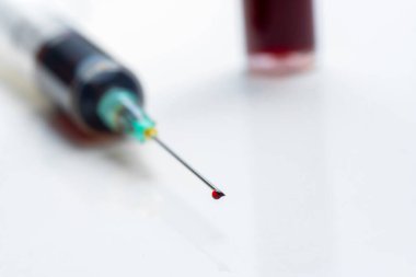 Şırınganın ucundaki kan damlası. Arka planda odaklanmamış bir kan testi tüpü var.