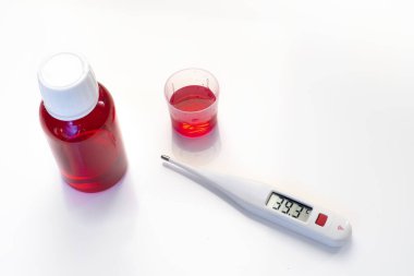 dijital termometre beyaz zemin üzerinde kullanmaya hazır bir şişe kırmızı şurupla ateş değerlerini gösteriyor