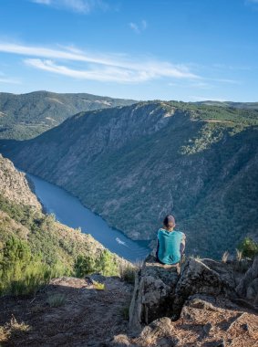 Çocuk, İspanya 'nın Ribeira Sacra şehrinde Sil nehrinin kıyısındaki bir uçurumun tepesinde bir kanyondan geçen bir gemi düşünüyor.