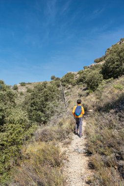 Çocuk, turuncu ceketli ve mavi sırt çantalı bir dağ yolunda yürüyordu.