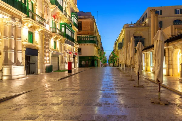 The main city street of the Republic in the light of lanterns at dawn. Valletta. — Stock Photo, Image