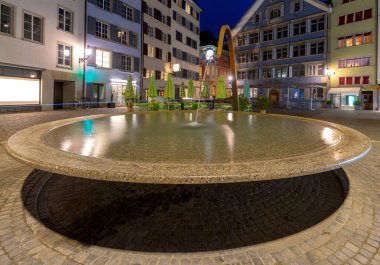 Zürih. Gece aydınlatmamunda Munsterhof Meydanı'nda çeşme.
