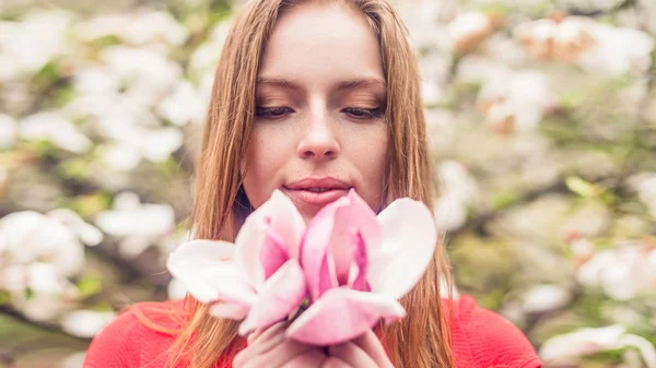 Linda chica con pecas sonriendo sobre un fondo de flores. La chica está en manos de Magnolia. Primer plano de la primavera . — Foto de Stock