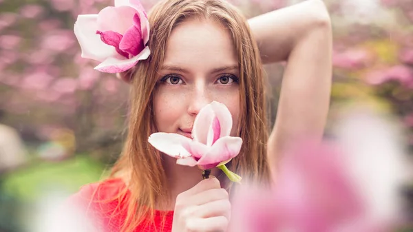 Linda chica con pecas sonriendo sobre un fondo de flores. Chica sostiene en las manos de magnolia y mirando a la cámara. Primer plano de la primavera . — Foto de Stock