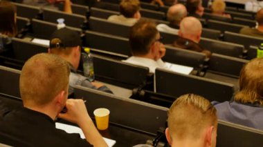 Öğrenciler konferans salonunun önünde öğretmeni dinliyorlar.