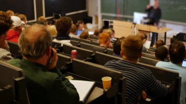 Öğrenciler konferans salonunun önünde öğretmeni dinliyorlar.