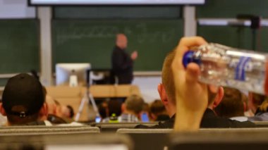 Öğrenciler konferans salonunun önünde öğretmeni dinliyorlar.