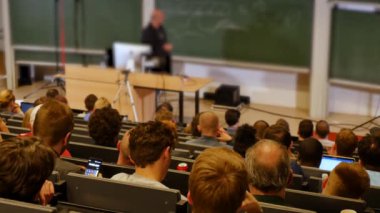 Öğrenciler konferans salonunun önünde öğretmeni dinliyorlar.