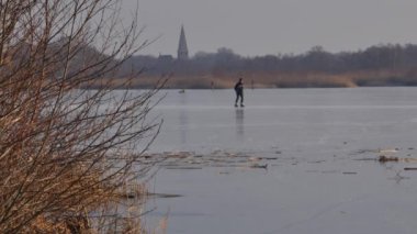 Gün batımında donmuş gölde paten süren insanların görüntüsü.