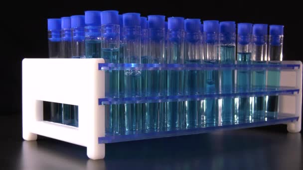 Tubes à essai avec liquide bleu tournant sur fond noir dans un laboratoire 4K