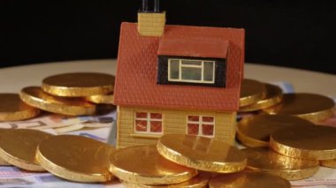 Oyuncak ev, siyah arka planda dönen Euro parasıyla çevrili.
