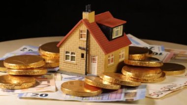 Oyuncak ev, siyah arka planda dönen Euro parasıyla çevrili.
