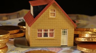 Oyuncak ev, siyah arka planda dönen Euro parasıyla çevrili.