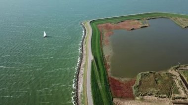 Hollanda 'daki IJsselmeer' de bir hendek ve göl kenarındaki bir yelkenlinin havası.