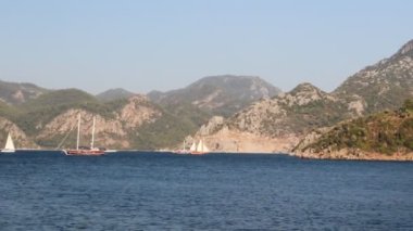 Güneşli bir günde deniz kıyısı ve dağların manzaralı görüntüleri.