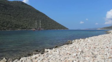 Yelkenli tekneleri, mavi deniz suyu ve çakıl taşı plajı olan güzel bir körfezin manzarası..