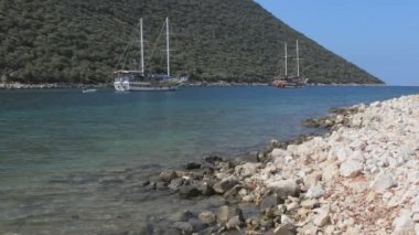 Yelkenli tekneleri, mavi deniz suyu ve çakıl taşı plajı olan güzel bir körfezin manzarası..