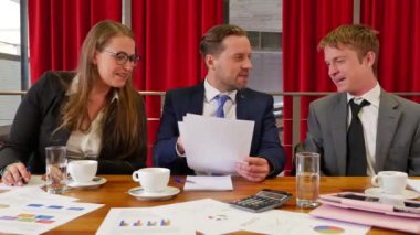 Üç iş ortağı konferans salonunda buluşuyor ve arka planda kırmızı perdeler var.