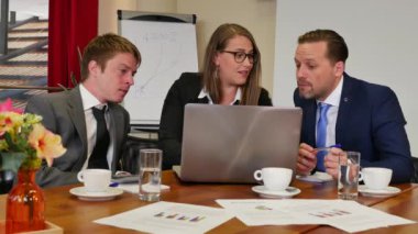 Üç iş ortağı konferans salonunda buluşuyor ve arka planda kırmızı perdeler var.