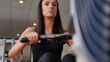 Güzel esmer bir kadının kürek makinesinde spor yaparken çekilmiş görüntüleri.