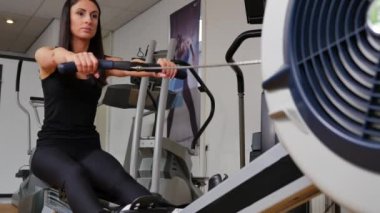 Güzel esmer bir kadının kürek makinesinde spor yaparken çekilmiş görüntüleri.