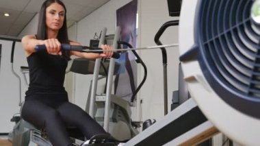 Güzel esmer bir kadının kürek makinesinde spor yaparken çekilmiş görüntüleri.