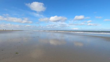 Hollanda 'daki Schiermonnikoog adasında bulut yansımaları ve büyük dalgalarla sahil ve deniz
