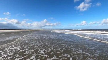 Hollanda 'daki Schiermonnikoog adasında bulut yansımaları ve büyük dalgalarla sahil ve deniz