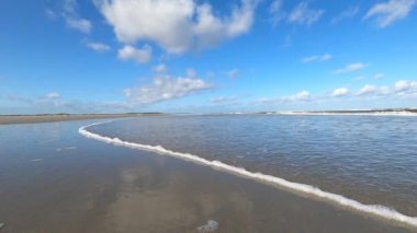 Hollanda 'daki Schiermonnikoog adasında bulut yansımaları ve büyük dalgalarla sahil ve deniz