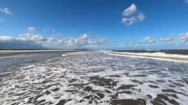 Hollanda 'daki Schiermonnikoog adasında bulut yansımaları ve büyük dalgalarla sahil ve deniz