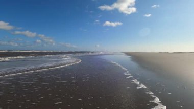 Hollanda 'daki Schiermonnikoog adasında bulut yansımaları ve büyük dalgalarla sahil ve deniz