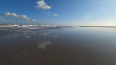 Hollanda 'daki Schiermonnikoog adasında bulut yansımaları ve büyük dalgalarla sahil ve deniz