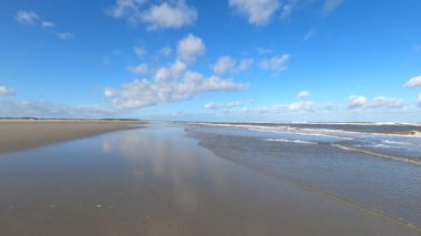 Hollanda 'daki Schiermonnikoog adasında bulut yansımaları ve büyük dalgalarla sahil ve deniz