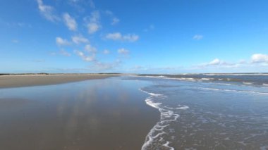 Hollanda 'daki Schiermonnikoog adasında bulut yansımaları ve büyük dalgalarla sahil ve deniz