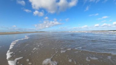 Hollanda 'daki Schiermonnikoog adasında bulut yansımaları ve büyük dalgalarla sahil ve deniz