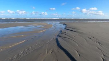 Hollanda 'daki Schiermonnikoog adasında bulut yansımaları ve büyük dalgalarla sahil ve deniz