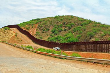 Border Fence beside a road near Nogales, Arizona separating the United States from Mexico with border patrol vehicle.  clipart